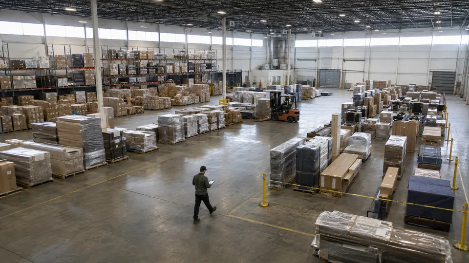 Warehouse floor with racked pallet storage on one side and wrapped freight staged for outbound transfer on the other